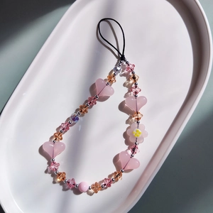 Détail de perles en forme de cœur et fleur sur une dragonne de téléphone rose