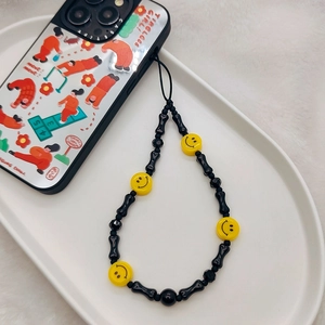 Close-up of beaded phone charm with black bone beads and yellow smiley faces on a tray