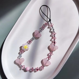 Dragonne de téléphone perlée avec cœurs roses et fleurs sur un plateau en céramique blanche