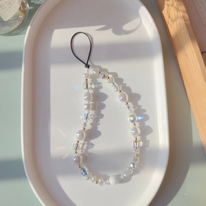 Detail of beaded phone strap with white pearls and iridescent crystals on a ceramic tray