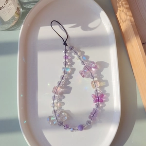 Detail of beaded phone strap with purple butterflies and crystal charms on white tray
