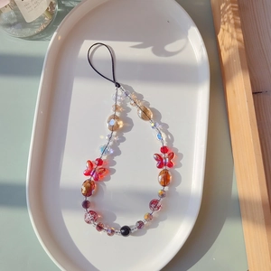 Macro detail of red butterfly beaded phone strap on white porcelain plate with soft shadows