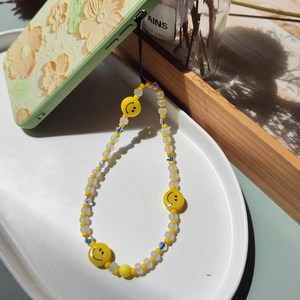 Beaded phone charm with yellow smiley faces on a green floral patterned phone case