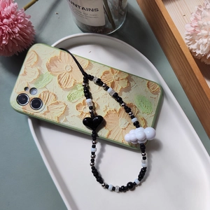 Detail of beaded phone strap with black heart and white cloud charms on a floral case