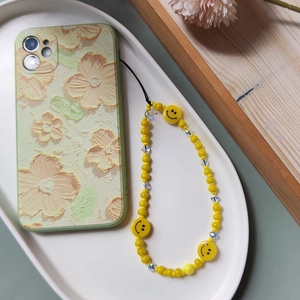 Detail of green floral embossed phone case with yellow smiley face beaded charm lanyard