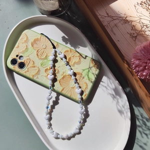 White heart-shaped beaded phone charm on a yellow floral case in a lifestyle setting