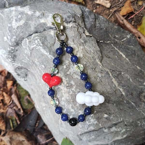 Detail of handmade beaded keychain with red heart and white cloud on natural rock background