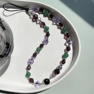 Colorful crystal beaded phone charm with purple crystal and green agate beads on a ceramic tray