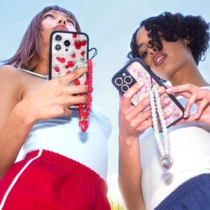 Outdoor shot showing vibrant strawberry and floral iPhone cases with beaded wrist straps