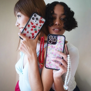 Close-up of beaded strawberry phone charms and floral cases on iPhone 15 Pro
