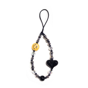 Detail of beaded phone charm with yellow smiley face, black heart, and silver bone charms