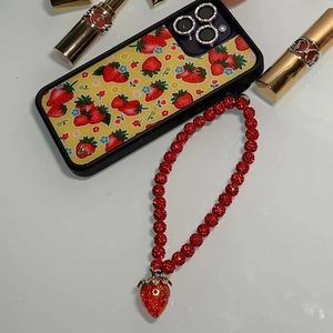 Detail of red beaded strawberry phone strap on yellow floral iPhone case with crystal decor