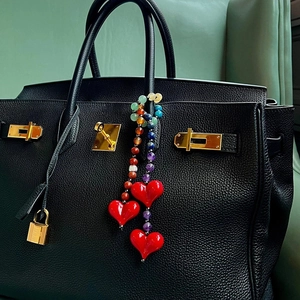 Detail of colorful gemstone beads and red heart charms on a black leather handbag strap