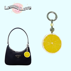 Detail of yellow acrylic lemon slice keychain attached to a black shoulder bag strap
