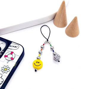 Bijou de téléphone perlé avec visage souriant et dé, accroché sur support bois