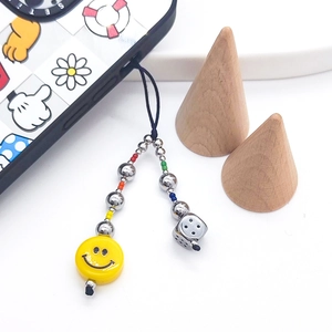 Bijou de téléphone perlé avec visage souriant et breloques de dés sur coque mobile
