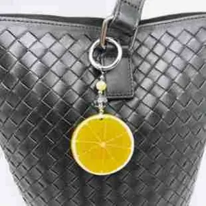Close-up of a lemon slice acrylic keychain with beads on a black woven bag