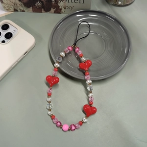 Beaded phone strap with red hearts and pearls displayed on a minimalist ceramic plate