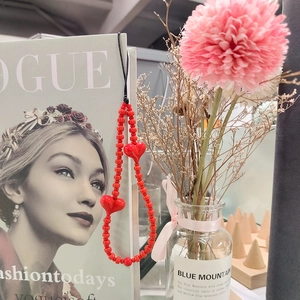 Red acrylic beaded phone strap with heart pendants displayed next to a fashion magazine