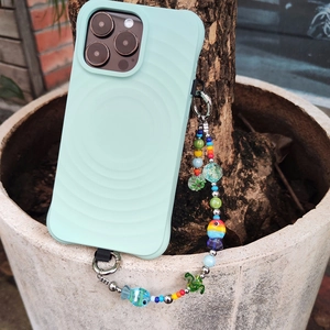 Mint green wavy phone case with colorful beaded fish charm strap in natural outdoor setting