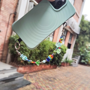 Colorful beaded phone strap with fish and flower charms held in a hand outdoors