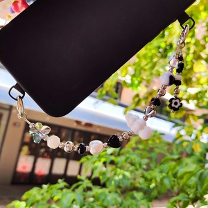 Beaded phone charm with white cloud and black stars attached to a black smartphone case