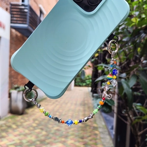 Colorful beaded phone strap with cat and fish charms on a blue case in nature