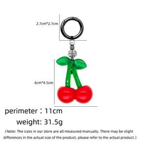 Detailed view of red cherry bag charm with green leaves and silver beads on a white background