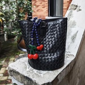 Black woven leather bucket bag detail with cherry and heart-shaped gemstone charms