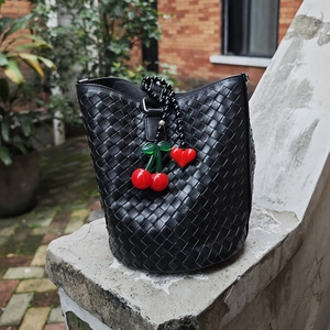 Detail of hand-woven black leather bucket bag with red cherry and heart bead charms
