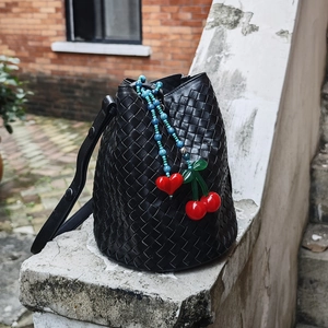 Detail of woven leather bucket bag with cherry and heart charms on a white stone ledge