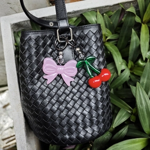 Detail of cherry and bow charms attached to a black woven bucket bag in natural light