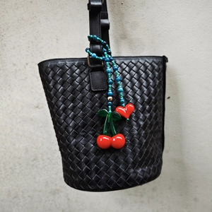 Close-up of woven leather bucket bag with colorful cherry and heart beaded charm