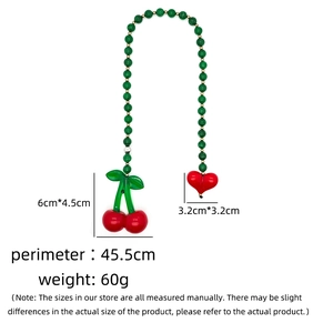 Detailed view of green beaded bag chain with red cherry and heart pendants shown on white back