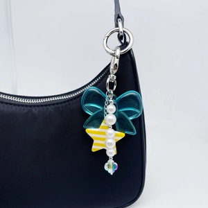 Blue bow phone charm with star pendant and pearls attached to a black bag handle