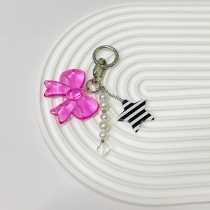 Detail of pink bow phone charm with white pearls and star pendant on a wavy tray