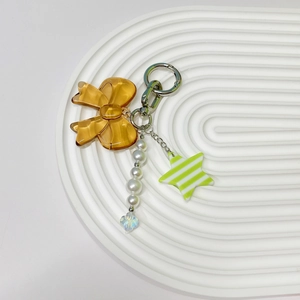 Detail of keychain featuring amber resin bow, pearl charms, and green striped star