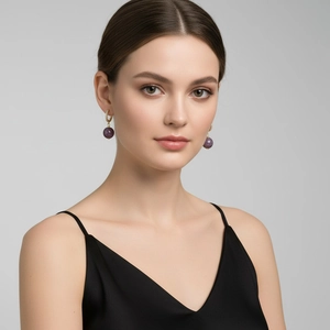 Detail of luxury gold earrings with pavé zircons and a purple gemstone drop on a model
