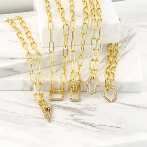 Close-up of golden paperclip chains with micro-inlaid zircon charms on marble