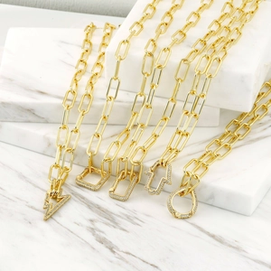Close-up of gold paperclip necklaces with various zircon pendants on marble stand