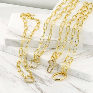 Detail of gold paperclip chain necklaces with micro-pave diamond pendants on marble