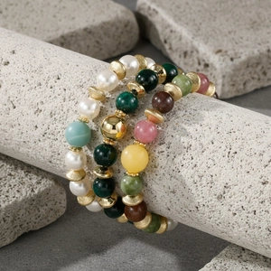 Meerlaagse kleurrijke edelsteen en parel armband met gouden tussenstukken detailopname.