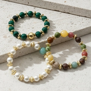 Close-up van kleurrijke toermalijn, parel en groene stenen kralen armbanden met gouden spacers.
