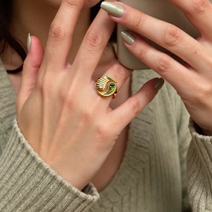 Golden Tai Chi style ring with green and white zircons worn on a model's finger