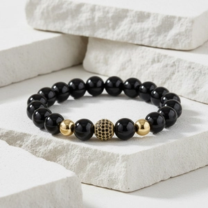 Detailed close-up of matte black beads and micro-pave gold crown charm on white stone blocks