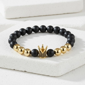Detail of matte black beads and golden crown charm with zircon on white stone