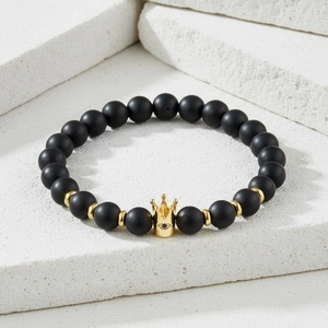 Close-up of black matte beaded bracelet with golden crown charm and blue gemstone detail