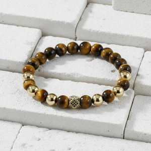 Detail view of tiger eye beads with gold micro-pave crown on white stone surface