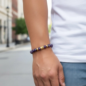 Detail of purple amethyst bead bracelet with textured gold metal tube on a wrist