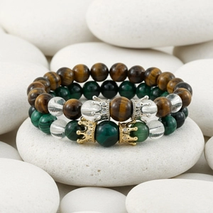 Close-up of lapis lazuli and tiger eye beaded bracelets with crown charms on pebbles